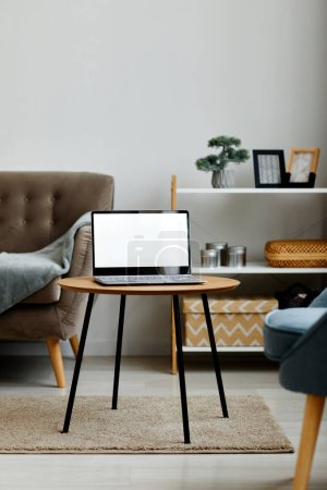 Photo for Vertical background image of opened laptop with blank white screen on coffee table in minimal living room interior, copy space - Royalty Free Image