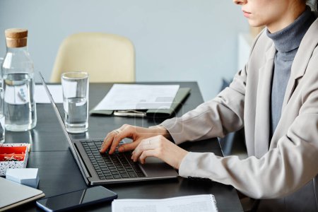 Téléchargez les photos : Vue de côté gros plan de la jeune femme utilisant un ordinateur à la table de réunion au bureau contre un mur bleu, espace de copie - en image libre de droit