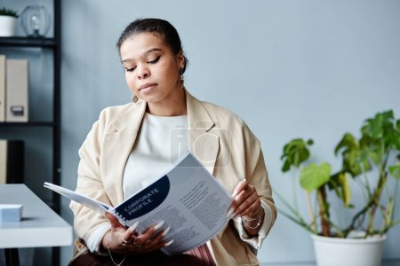 Téléchargez les photos : Portrait minimal de la jeune femme d'affaires noire lisant le rapport sur le lieu de travail dans le bureau sur fond gris, espace de copie - en image libre de droit