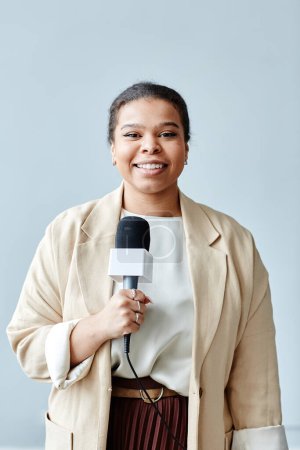 Foto de Retrato mínimo de una periodista sonriente sosteniendo el micrófono mientras reporta noticias y mira la cámara - Imagen libre de derechos