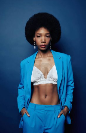 Foto de Mínima toma vertical de la joven mujer negra con el pelo natural vistiendo traje azul vibrante y mirando a la cámara con confianza - Imagen libre de derechos