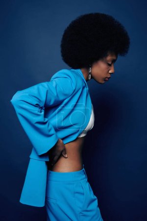 Foto de Mínima foto de vista lateral de una joven mujer negra con cabello natural que viste un traje azul vibrante y posa con elegancia - Imagen libre de derechos