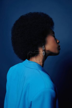 Téléchargez les photos : Minimal coup de mode de jeune femme noire avec des cheveux naturels gonflés posant sur fond bleu - en image libre de droit