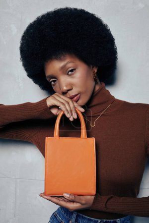 Photo for Vertical shot of black fashion model with puffy natural hair holding trendy handbag to camera - Royalty Free Image