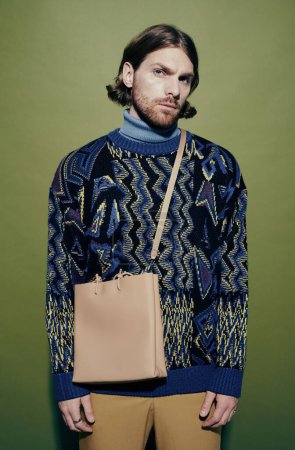 Téléchargez les photos : Portrait vertical du mannequin masculin portant un pull tendance et un sac bandoulière sur fond vert - en image libre de droit