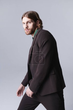 Foto de Retrato mínimo del modelo de moda masculino con traje en tonos marrones terrosos y mirando a la cámara contra el gris - Imagen libre de derechos