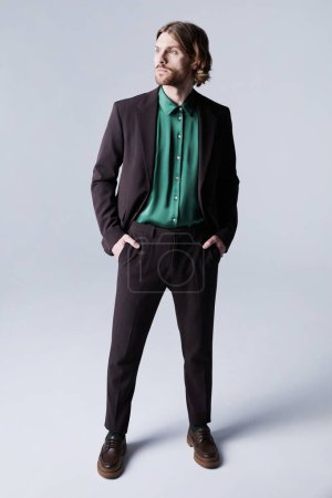 Foto de Retrato de cuerpo entero de modelo de moda masculino con traje en tonos marrones terrosos y mirando hacia otro lado contra el gris - Imagen libre de derechos