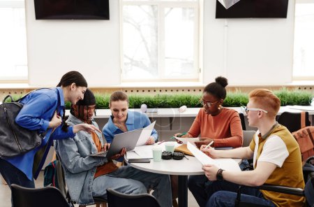 Foto de Diverso grupo de estudiantes universitarios que estudian juntos en la mesa redonda y discuten el proyecto, espacio para copiar - Imagen libre de derechos