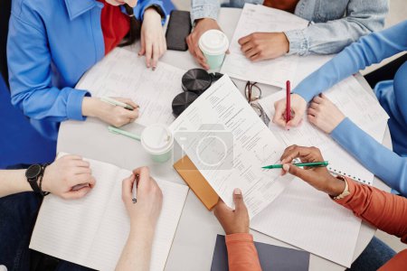 Photo for Top view of table with notebooks and documents busy group of college students preparing for exams - Royalty Free Image