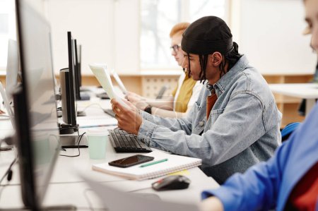 Foto de Retrato de vista lateral de un joven negro usando una computadora en la biblioteca de la universidad mientras investigaba para exámenes con un grupo de personas en fila - Imagen libre de derechos