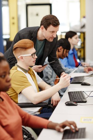 Foto de Retrato vertical vibrante del profesor masculino que ayuda al estudiante a usar la computadora en el aula de la universidad - Imagen libre de derechos
