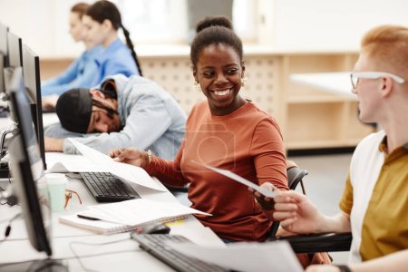 Foto de Vibrante retrato de una mujer afroamericana sonriente entregando notas a un amigo en clase mientras estudian juntos en la universidad - Imagen libre de derechos