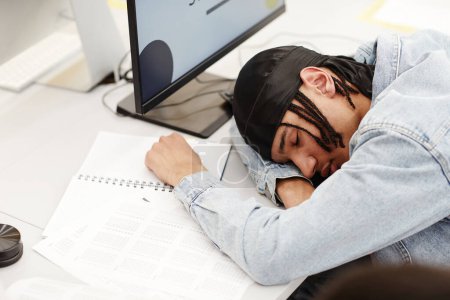 Téléchargez les photos : Minimal portrait grand angle de jeune étudiant noir dormant sur le bureau dans la salle de classe du collège par ordinateur - en image libre de droit