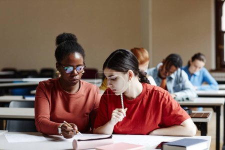 Téléchargez les photos : Portrait de face de deux jeunes femmes prenant des notes tout en étudiant dans une salle de classe collégiale, espace de copie - en image libre de droit