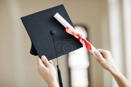 Photo for Close up of hands holding graduation cap and diploma with red ribbon at ceremony - Royalty Free Image