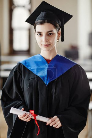 Photo for Vertical portrait of young woman wearing graduation gown and smiling at camera - Royalty Free Image