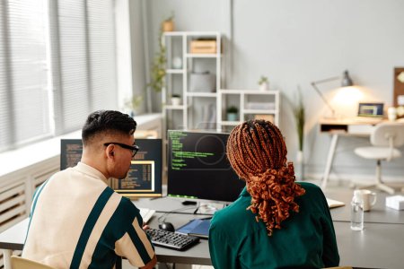 Téléchargez les photos : Vue arrière portrait de deux développeurs informatiques utilisant l'ordinateur tout en examinant le code de programmation dans le bureau, l'espace de copie - en image libre de droit