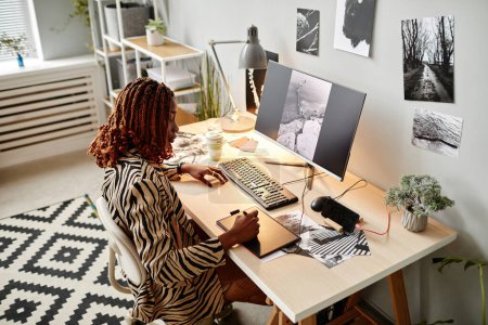 Téléchargez les photos : Portrait grand angle de créatrice noire éditant des photographies au bureau à domicile avec des impressions graphiques, espace de copie - en image libre de droit