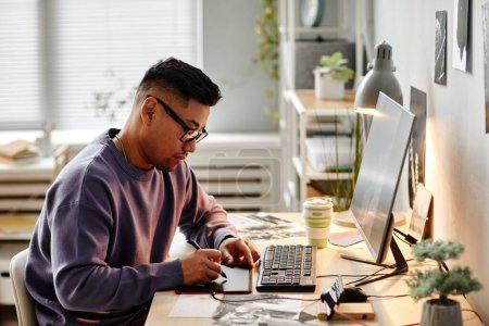 Téléchargez les photos : Portrait de créateur masculin asiatique retoucher des photos au bureau à la maison et en utilisant une tablette stylo - en image libre de droit