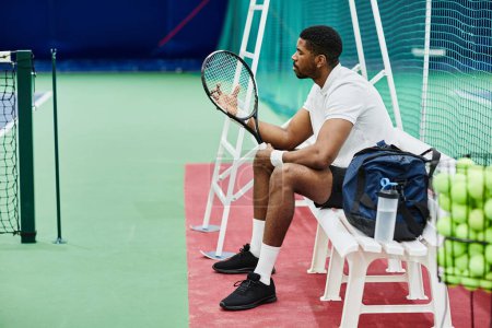 Téléchargez les photos : Portrait latéral d'un joueur de tennis professionnel tenant une raquette tout en prenant une pause sur un banc au tribunal, espace de copie - en image libre de droit