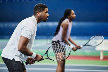 Photo for Side view portrait of two young African American people playing tennis at indoor court, copy space - Royalty Free Image