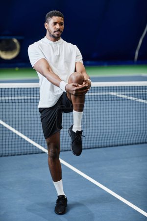 Photo for Full length portrait of young black sportsman stretching while preparing for tennis game at indoor court - Royalty Free Image