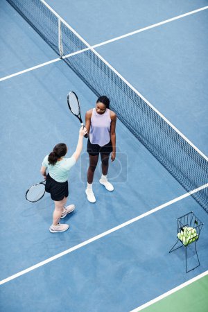 Foto de Vista superior vertical del entrenador de tenis femenino que trabaja con el cliente contra el suelo de la cancha azul, espacio de copia - Imagen libre de derechos
