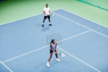 Téléchargez les photos : Plan minimaliste en angle élevé du couple afro-américain jouant au tennis en couple à l'intérieur du terrain, espace de copie - en image libre de droit