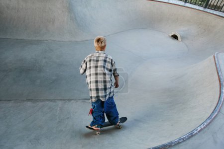 Téléchargez les photos : Vue arrière du jeune garçon à cheval skateboard au skatepark extérieur en zone urbaine, espace de copie - en image libre de droit