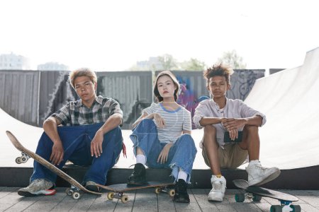 Téléchargez les photos : Portrait complet de trois locataires dans satepark assis sur la rampe et regardant la caméra en milieu urbain - en image libre de droit