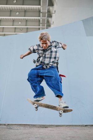 Foto de Mínima acción de tiro de joven adolescente monopatín en el área urbana al aire libre y saltar en el aire haciendo trucos - Imagen libre de derechos