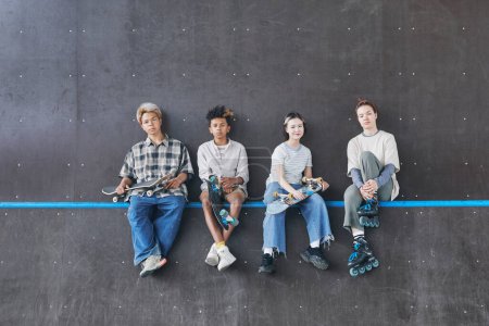 Foto de Mínimo gran angular de tiro de diverso grupo de adolescentes sentados en la rampa en el parque de skate y mirando a la cámara, espacio de copia - Imagen libre de derechos