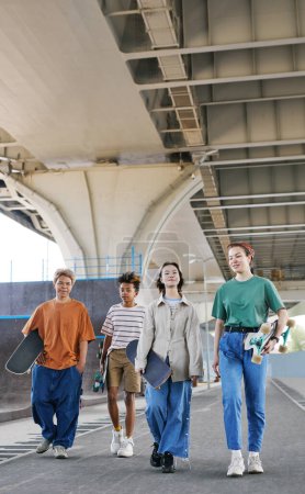 Foto de Largura completa de tiro de diverso grupo de adolescentes en skatepark al aire libre en el área urbana vistiendo trajes deportivos - Imagen libre de derechos