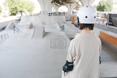 Foto de Vista posterior de la joven adolescente con protectores y casco en el parque de patinaje al aire libre, espacio para copiar - Imagen libre de derechos