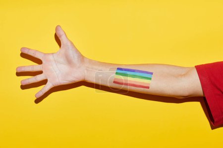 Foto de Vibrante foto amarilla del brazo con el tatuaje de la bandera del arco iris como símbolo del mes del orgullo LGBTQ - Imagen libre de derechos