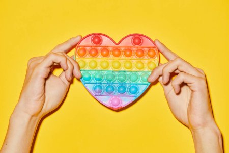 Téléchargez les photos : Plan vibrant de mains féminines tenant le cœur arc-en-ciel sur fond jaune comme symbole du mois de fierté LGBTQ - en image libre de droit
