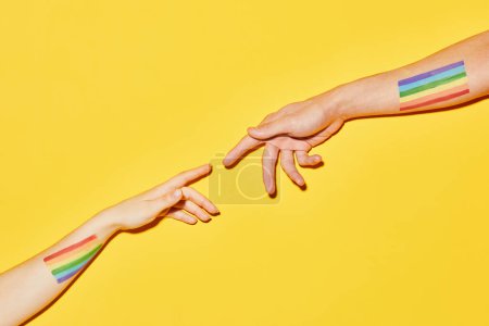 Téléchargez les photos : Plan vibrant de deux mains tendues avec des drapeaux LGBT sur fond jaune Style de création - en image libre de droit