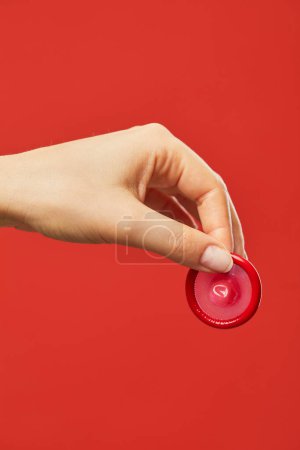 Téléchargez les photos : Gros plan vibrant de la main féminine tenant préservatif sur fond rouge sexe sûr et concept de protection - en image libre de droit