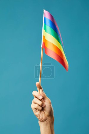 Téléchargez les photos : Plan vibrant de la main féminine tenant drapeau arc-en-ciel à fond bleu comme symbole de la fierté mois lgbtq - en image libre de droit