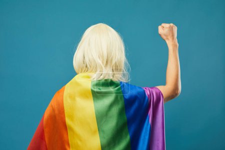 Foto de Vista posterior de la persona con bandera del arco iris contra vibrantes derechos LGBTQ de fondo azul - Imagen libre de derechos