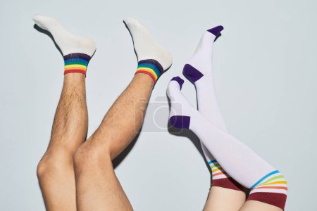 Mínimo tiro de juguetona pareja joven con calcetines con arcoíris símbolos pies arriba, espacio de copia