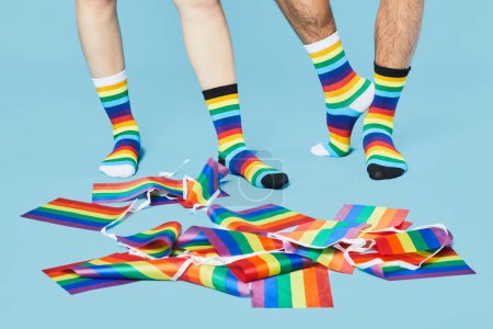 Téléchargez les photos : Plan minimal du couple portant des chaussettes arc-en-ciel avec des drapeaux LGBTQ sur fond bleu pastel, espace de copie - en image libre de droit