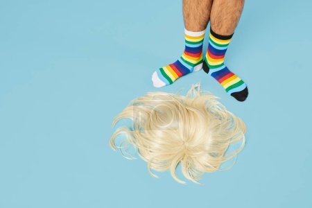 Foto de Mínimo tiro de hombre con calcetines de arco iris con peluca rubia en el suelo en el fondo azul pastel, espacio de copia - Imagen libre de derechos