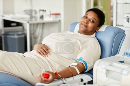 Photo for Portrait of smiling woman giving blood while laying in chair at blood donation center and looking at camera - Royalty Free Image