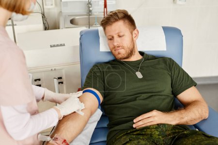 Téléchargez les photos : Portrait d'un jeune militaire qui donne du sang au centre des donneurs avec l'aide d'une infirmière, photocopier l'espace - en image libre de droit
