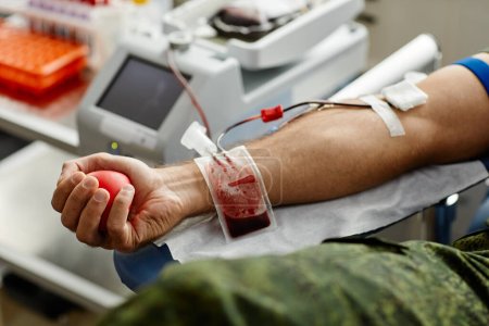 Foto de Primer plano de donante masculino irreconocible donando sangre y apretando la bola de estrés, espacio de copia - Imagen libre de derechos
