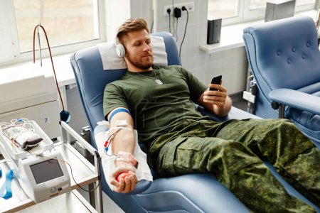 Téléchargez les photos : Portrait en grand angle d'un jeune homme souriant faisant don de sang dans le confort et regardant des vidéos sur smartphone, copier l'espace - en image libre de droit