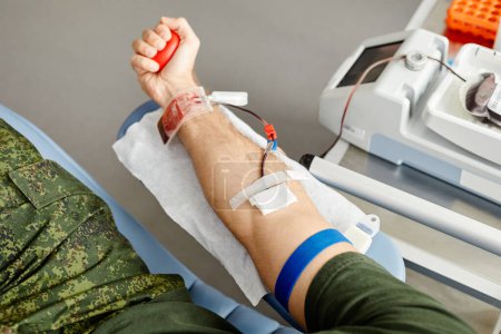 Téléchargez les photos : Vue du dessus du donneur mâle donnant du sang et tenant la balle de stress rouge dans la main au centre de don, espace de copie - en image libre de droit