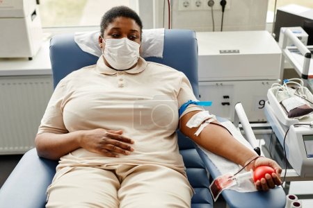Téléchargez les photos : Portrait de jeune femme noire faisant un don de sang alors qu'elle était allongée sur une chaise et portant un masque, espace de copie - en image libre de droit