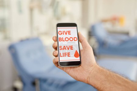 Photo for Close up of male blood donor holding smartphone with Give blood save life slogan at donation center, copy space - Royalty Free Image